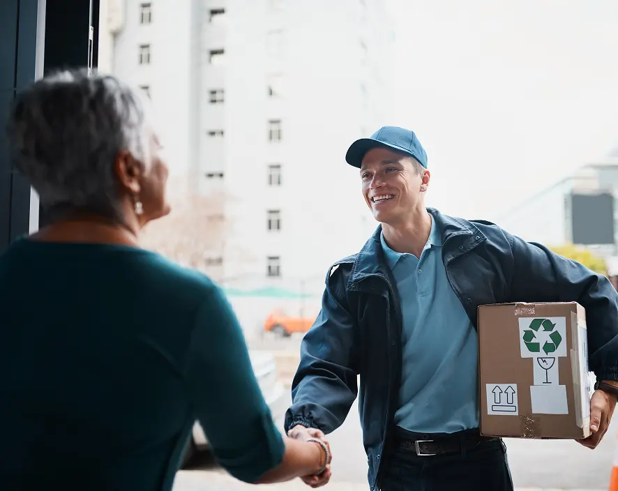 Delivery courier holding a cardboard box and shaking hands with a customer at the door.