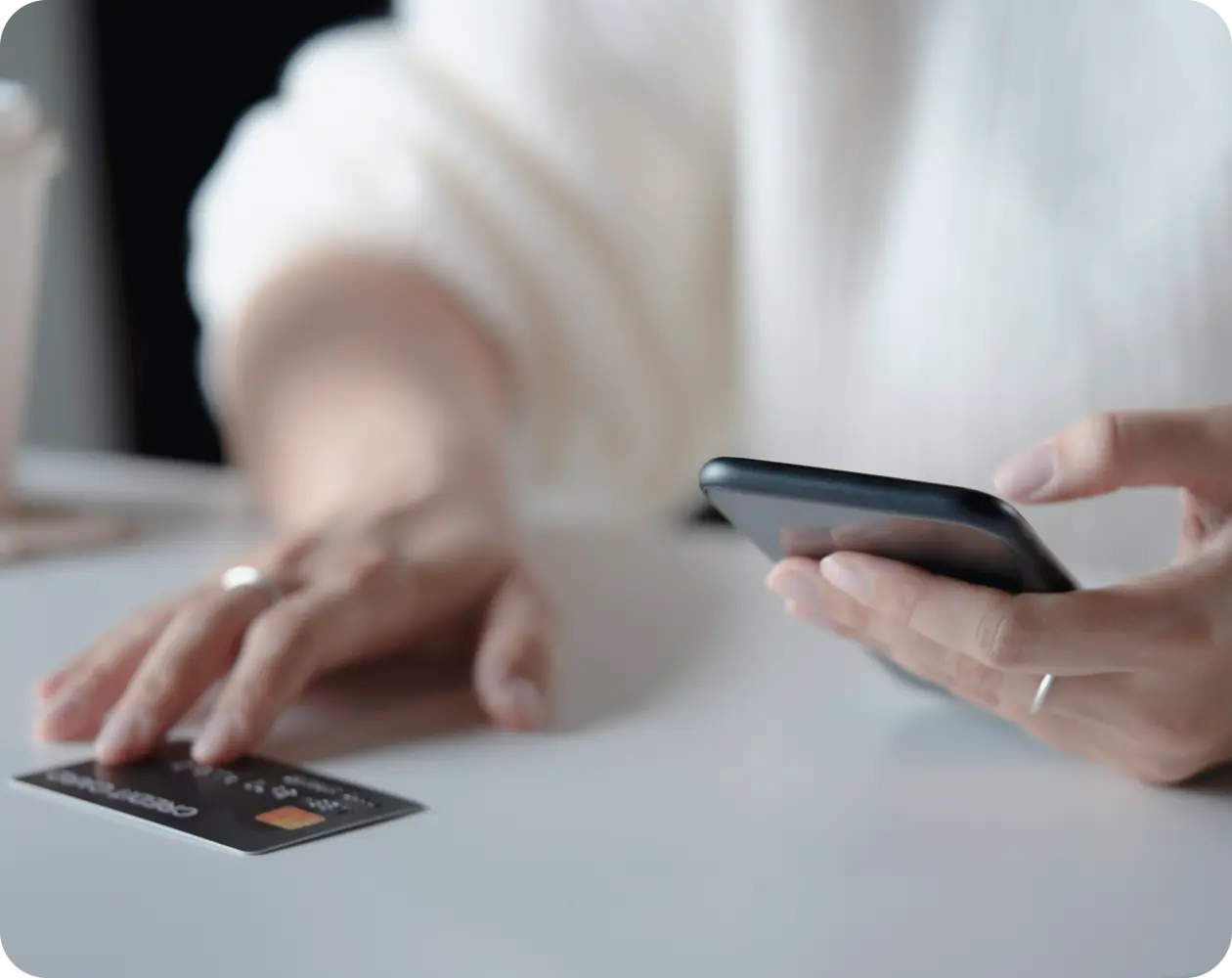 Person holding a phone with a bank card lying on the table.