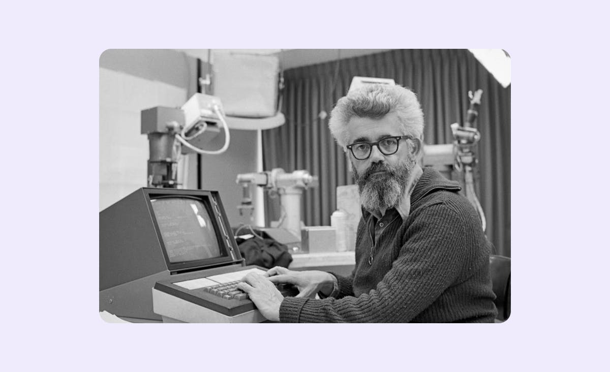 The photograph features John McCarthy, a professor of computer science in the artificial intelligence lab at Stanford in 1974. He is sitting at a computer, partially turned towards it.