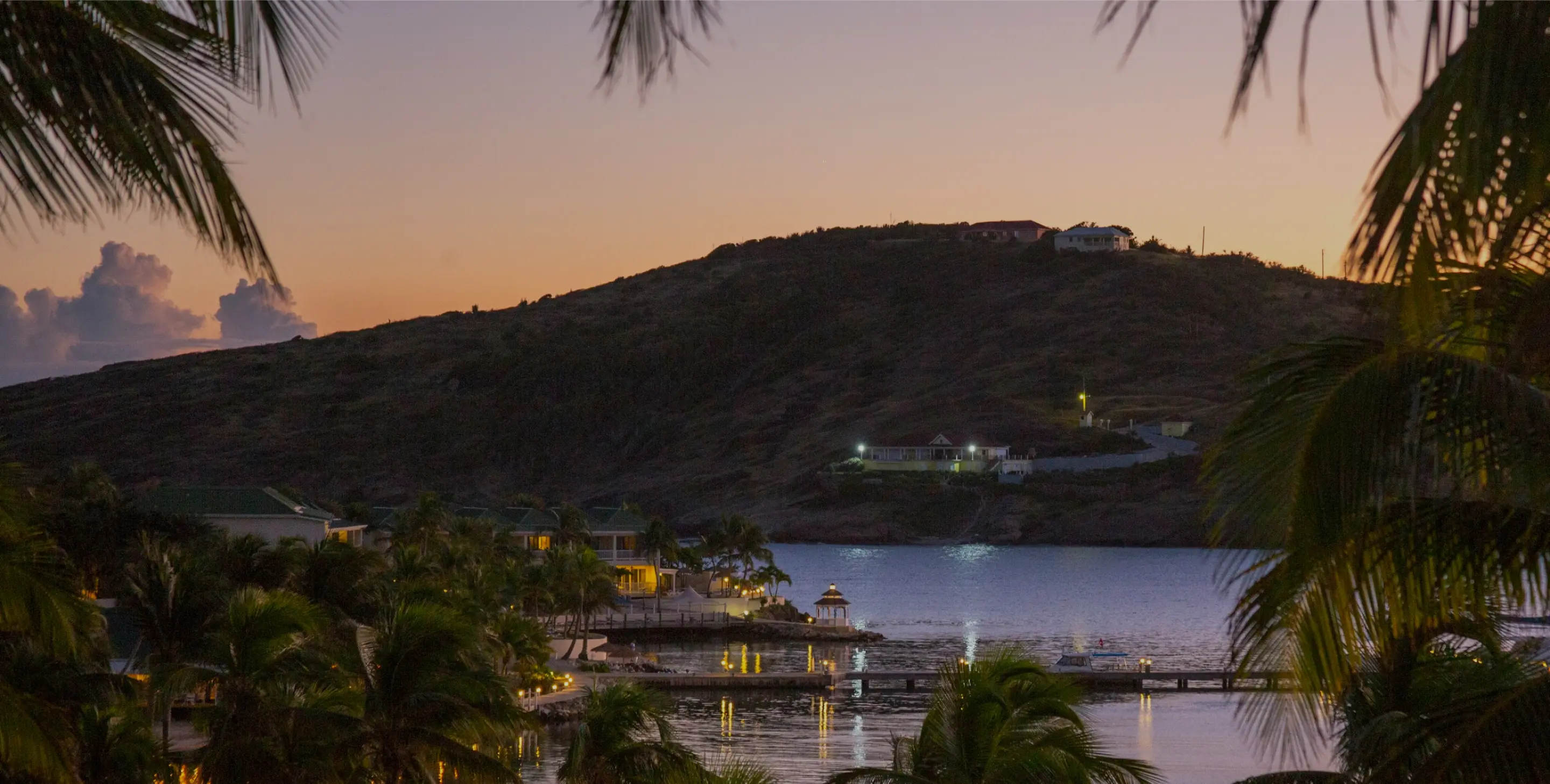 Coastal resort and palm trees at dusk overlooking a calm bay.