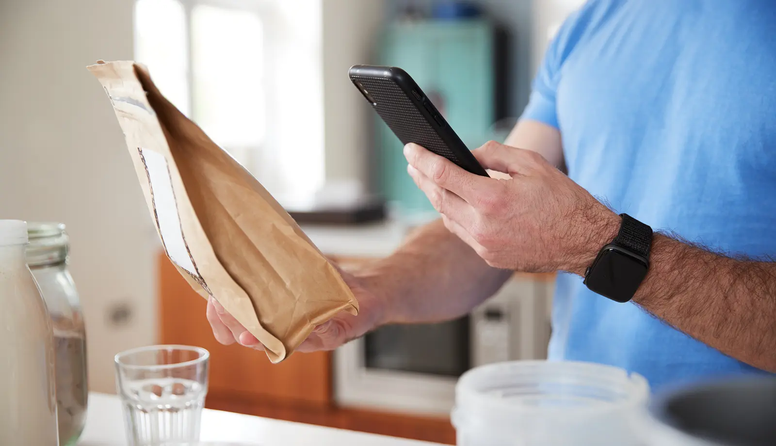 Person holding a paper meal bag in one hand and a smartphone in the other to scan its QR code.