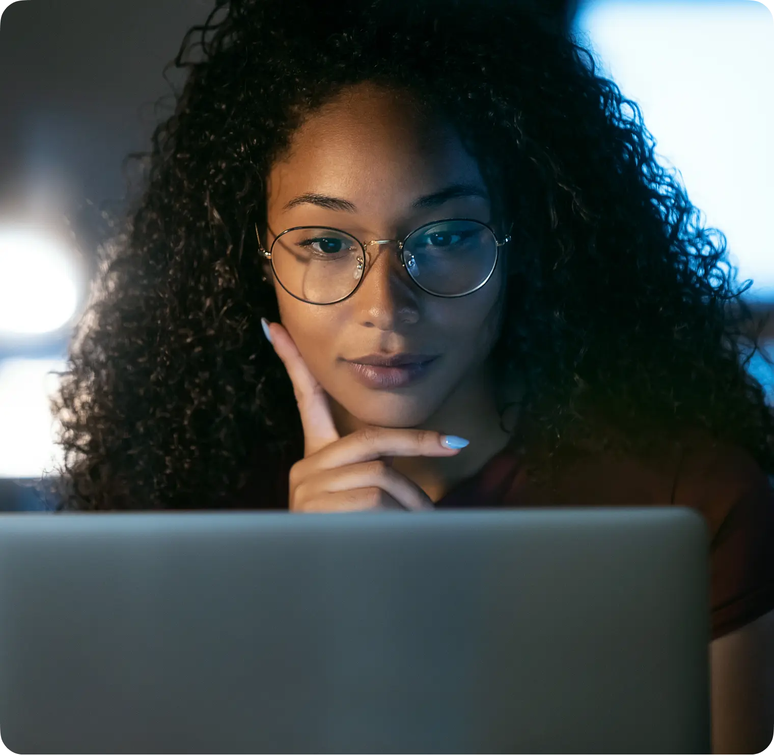 Woman in glasses focused on her laptop screen in a dark room.