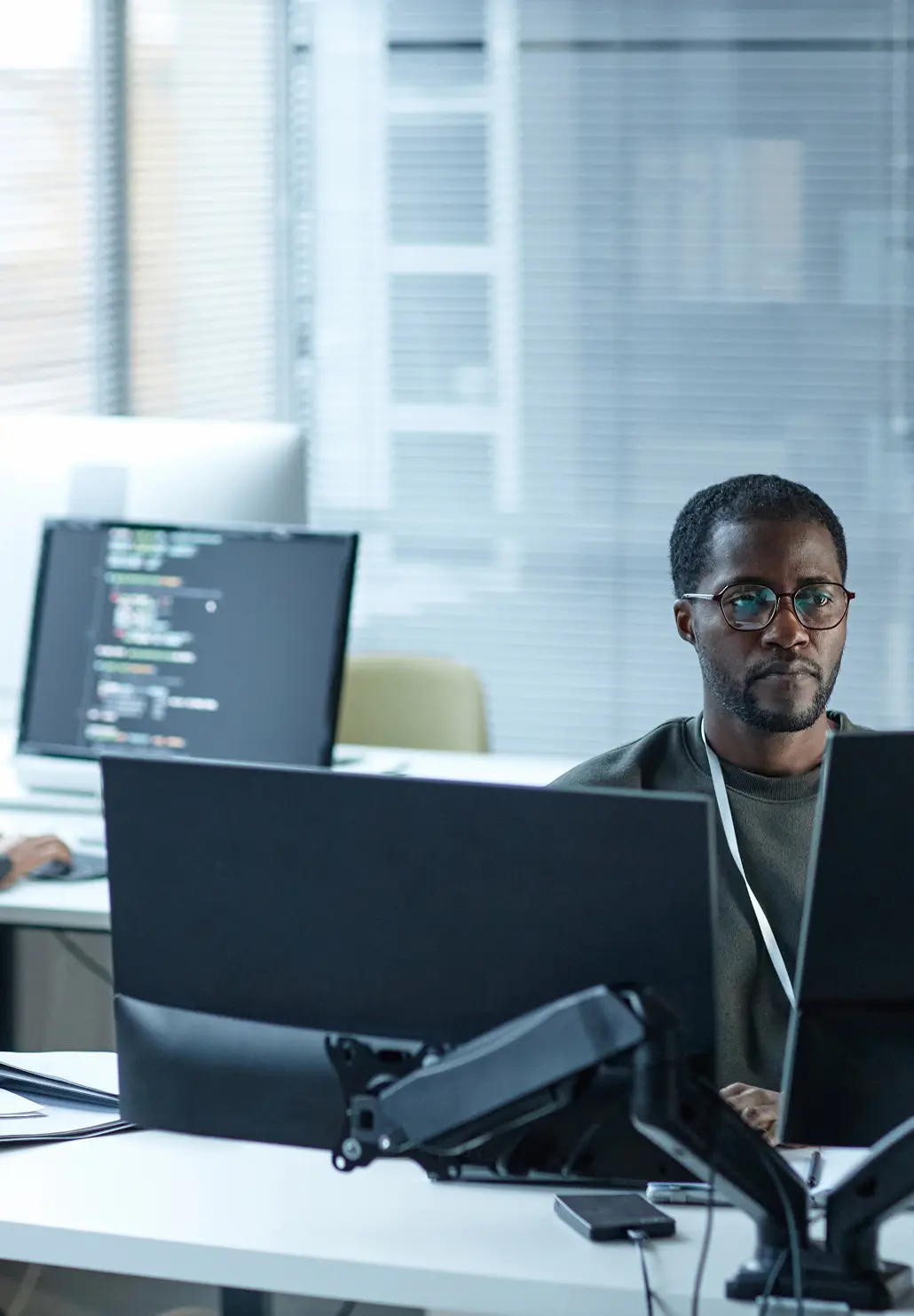Developer at a multi-monitor workstation reviewing code in a bright office.
