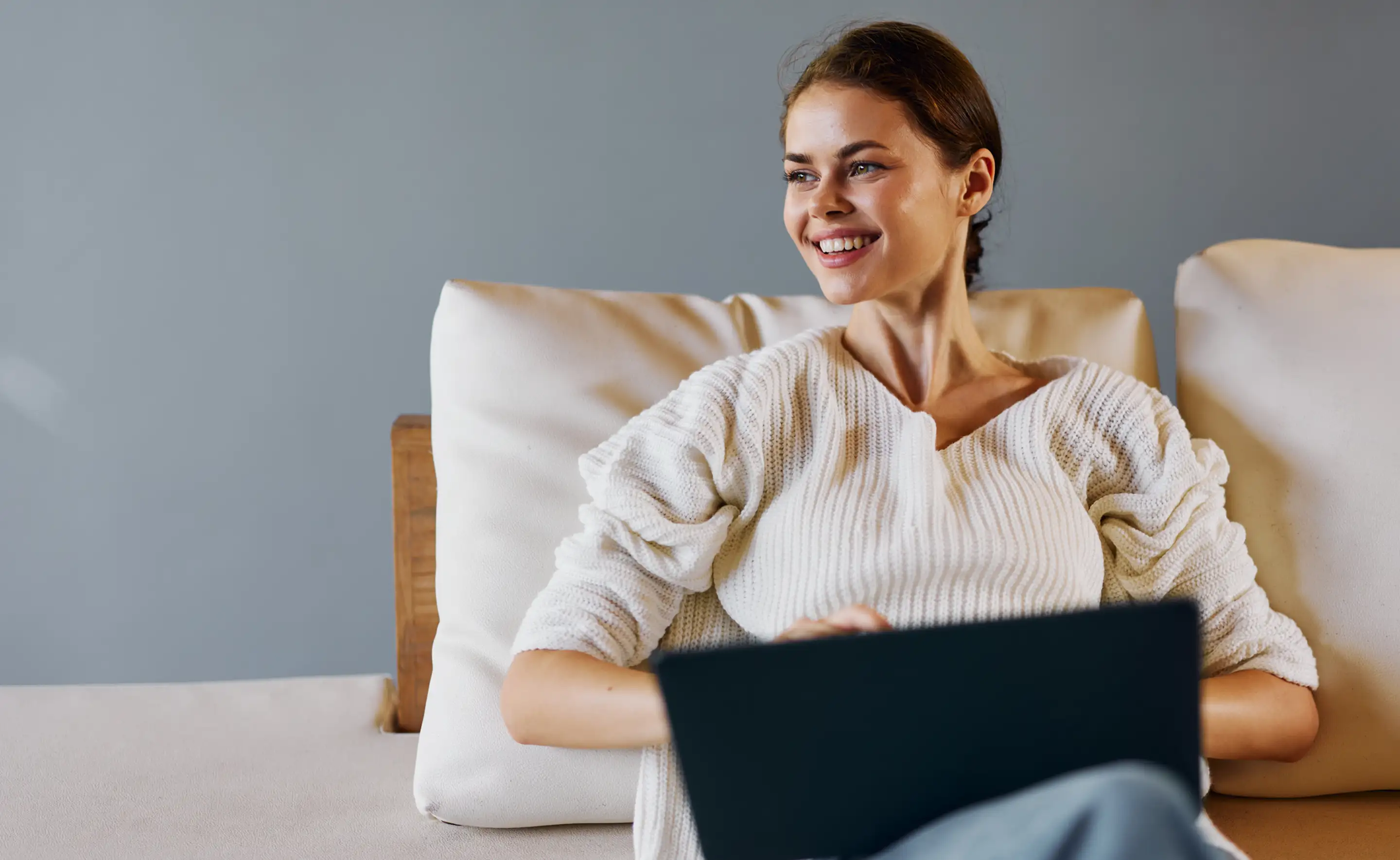 Smiling woman relaxing on a sofa with an open laptop.
