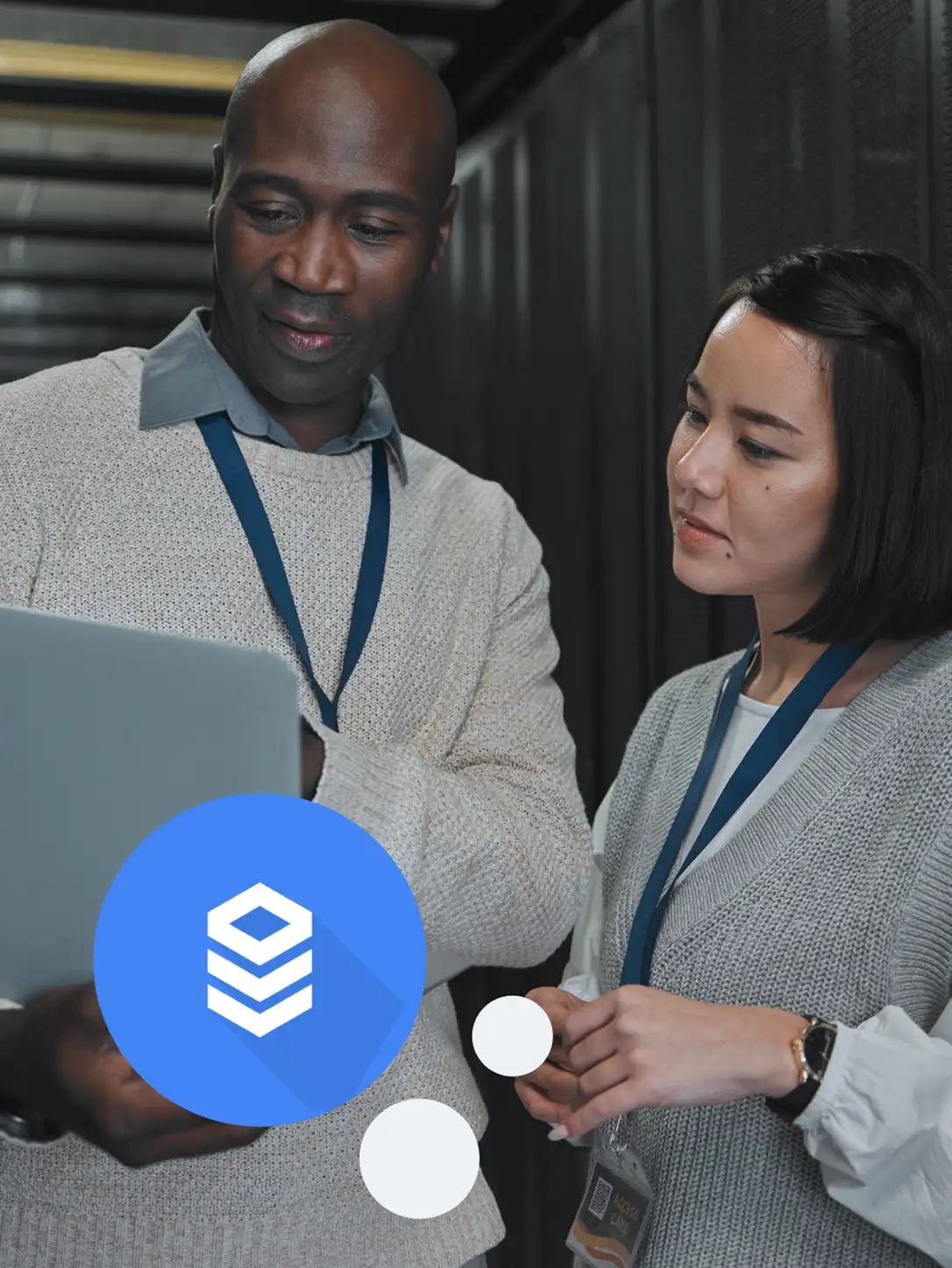 Two colleagues with access badges checking a laptop in a server room, with a database icon.